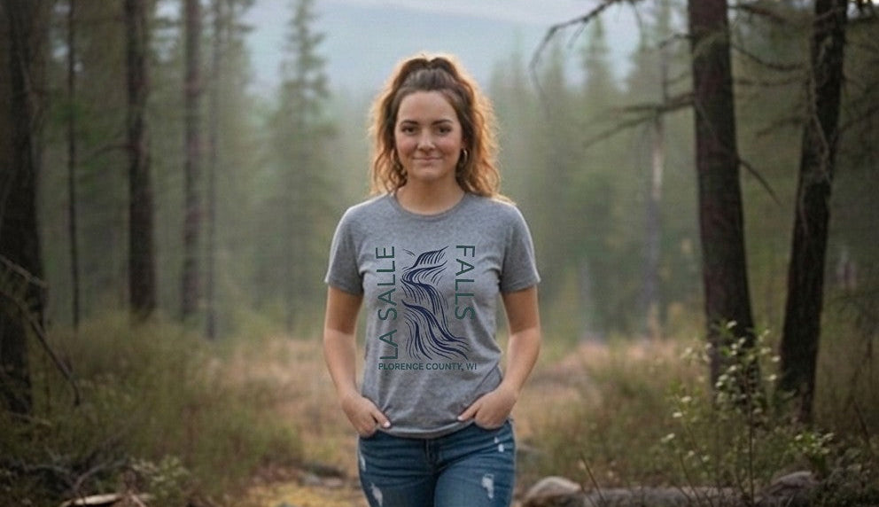 Woman walking through a forest wearing a gray t-shirt and jeans.